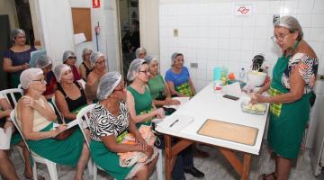 professora mostra a alunas sentadas materiais de curso #paratodosverem