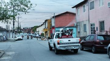 Carro fumacê percorre rua e lança fumaça para o lado direito. #Paratodosverem