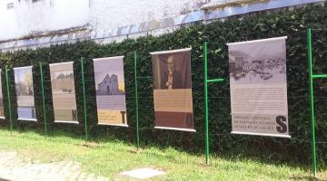 Paineis com imagens estão pendurados em sarrafos instalados em jardim. #paratodosverem 