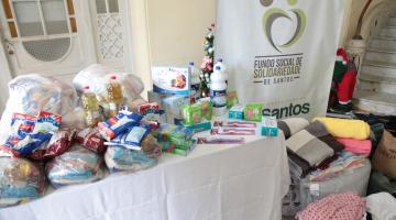 mesa com várias doações de alimentos e roupas empilhadas ao lado #paratodosverem