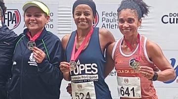 Três mulheres no pódio. A do centro é Ivanilda Pereira dos Santos, com a medalha no peito. #paratodosverem