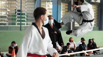 Mestre e atleta observam lutador executando golpe no alto #paratodosverem