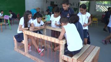 crianças estão sentadas em estrutura de madeira disputando uma bola com os pés no chão. #paratodosverem 
