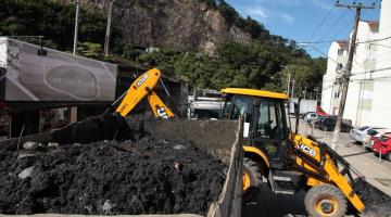 trator está ao fundo e ao lado de uma caçamba onde está depositado grande volume de resíduos. #paratodosverem 