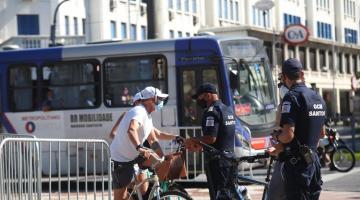 Dois guardas municipais abordam ciclista em ciclovia. Um ônibus passa atrás. #paratodosverem