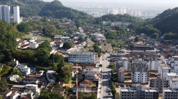 vista aérea por drone do morro, com várias edificações, uma igreja ao centro, e morros ao fundo. #paratodosverem