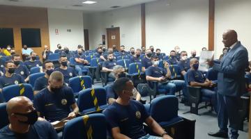 guardas estão sentados em auditório, respeitando o distanciamento, e assistindo palestra de um homem que está em pé. #paratodosverem