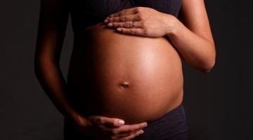 imagem em close de barriga de gestante com as mãos da mulher, uma abaixo e outra acima da barriga. #paratodosverem