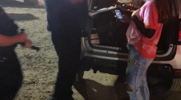 guarda municipal está na faixa de areia junto a uma mulher e um carro com o bagageiro aberto. Dentro há um equipamento de som. #paratodosverem