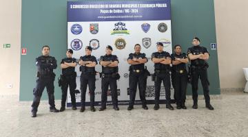 grupo de oito integrantes da guarda uniformizados e diante de um painel do evento. #paratodosverem