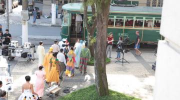 gravação de filme em praça de santos com equipamentos de filmagem e pessoas com roupas de época. bonde compõe o ambiente. #paratodosverem