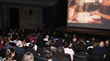 plateia lotada assistindo a filme projetado na tela. #paratodosverem