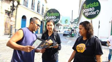 Duas guias de turismo estão na rua conversando com um homem. #paratodosverem