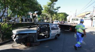 veículo parcialmente destruído é guinchado em avenida. Canal está ao lado. Agente da CET está do outro, na pista. #paratodosverem