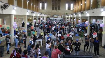 área interna do mercado muncipal lotada de pessoas. Bandeirinhas juninas decoram o ambiente penduradas entre as laterais do prédio. #paratodosverem