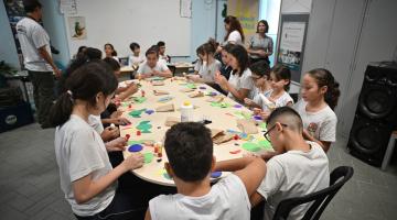 alunos recortam papeis em cima de mesa. #paratodosverem