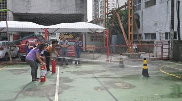 duas pessoas seguram extintos emitindo jato para ponto sinalizado em quadro em simulação para apagar incêndio. #paratodosverem