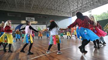 pessoas com roupas juninas dançam em roda. #paratodosverem