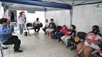 mulher em pé se apresenta para público sob tenda. #paratodosverem 