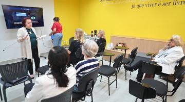mulher em pé fala a outras que estão sentadas. #paratodosverem