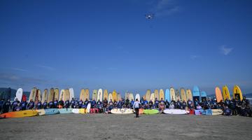 alunos com pranchas na faixa de areia em semi-círculo. #paratodosverem