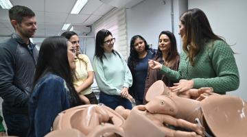 mulher orienta profissionais diante de modelos de borracha. #paratodosverem