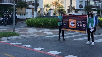 duas pessoas estão segurando faixa no centro de avenida. #paratodosverem