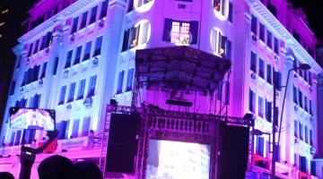 Fachada do hotel iluminada com palco à frente. #paratodosverem