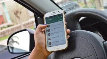 Mão está com celular ao volante #pracegover 