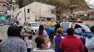 #pracegover Carro da Guarda Municipal leva imagem da santa por rua da cidade, observado por cerca de dez pessoas