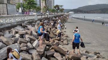 pessoas recolhem lixo em pedras na praia #paratodosverem