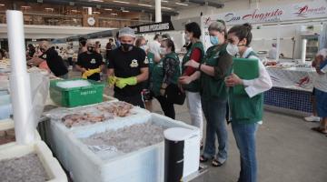 Fiscais uniformizados estão diante de caixas de pescado. #Paratodosverem