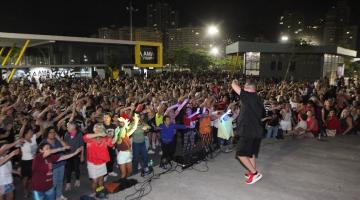 público dança diante de palco animado por instrutor. #paratodosverem