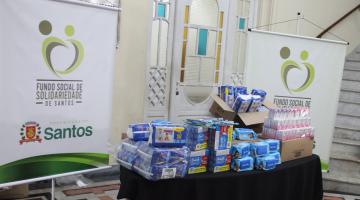 alimentos e fraldas sobre uma mesa e banner do fundo social. #paratodosverem