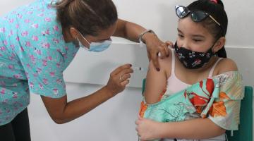 Mulher está vacinando menina. Ambas usam máscara. #paratodosverem