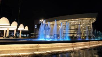 Foto noturna do centro de convenções com chafariz iluminado em azul a frente. #paratodosverem