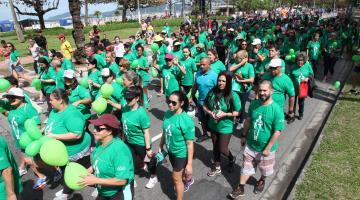 Pessoas vestidas com camisetas verdes caminham pela avenida da orla. #Pracegover