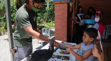 homem entrega gibi para crianças e ave está na mesa #paratodosverem