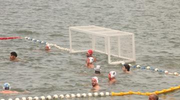 quadra de polo aquático no mar, com atletas na água e a trave no fundo. #paratodosverem 