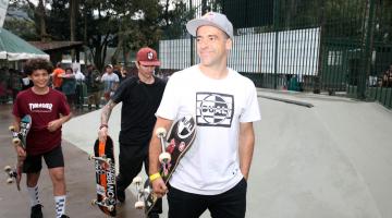 À frente da pista, Mineirinho posa com skate na mão e dois adolescentes atrás