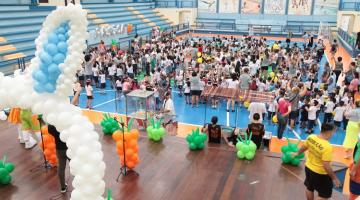muitas crianças em ginásio todo decorado com balões coloridos. #paratodosverem