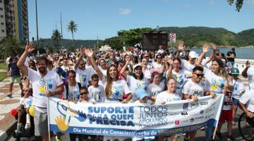 pessoas caminham com camisetas iguais e segurando uma faixa. #paratodosverem 