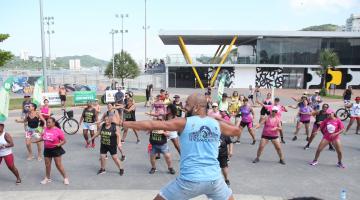 professor faz movimento que é repetido pelo público ao fundo. #paratodosverem 