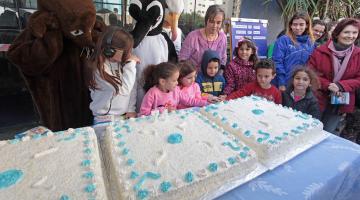 Crianças cantam parabéns diante de bolo e acompanhadas por grandes bonecos de animais marinhos. #Pracegover