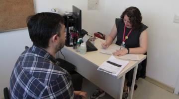 homem está de costas conversando com uma mulher que está fazendo anotações em um papel. #paratodosverem