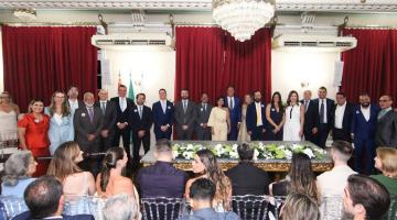 secretários, vice prefeita e prefeito em pé, posam para foto em auditório, com público sentado. #paratodosverem 