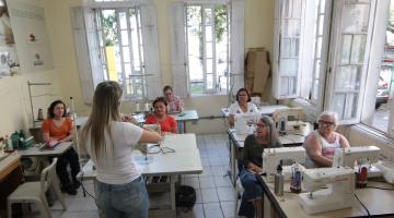 mulheres em sala de aula diante de máquinas de costura. #paratodosverem 