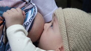 bebê olha para a mãe enquanto mama no peito #paratodosverem