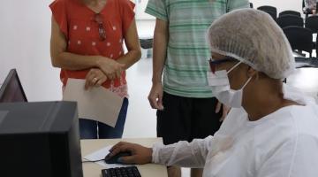 Pacientes em pé observam profissional de saúde operando computador. #pratodosverem