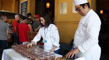 homem e mulher com roupas de chefs mexem em alimentos expostos #pracegover 